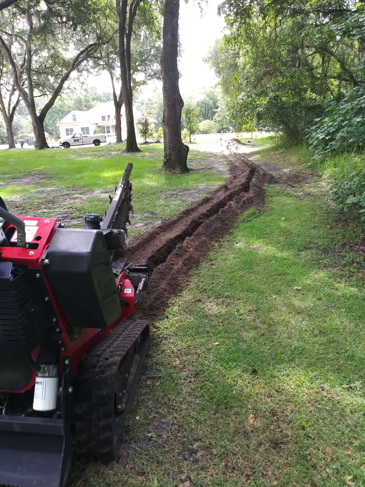 A walk-behind trencher cutting a long irrigation trench across a shaded lawn