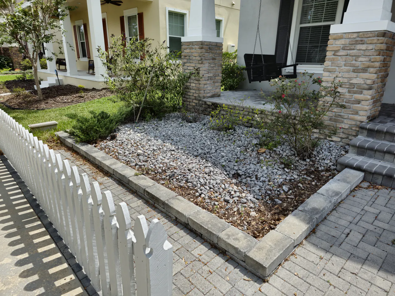 A sparse gravel bed with bare shrubs behind a white picket fence before new planting