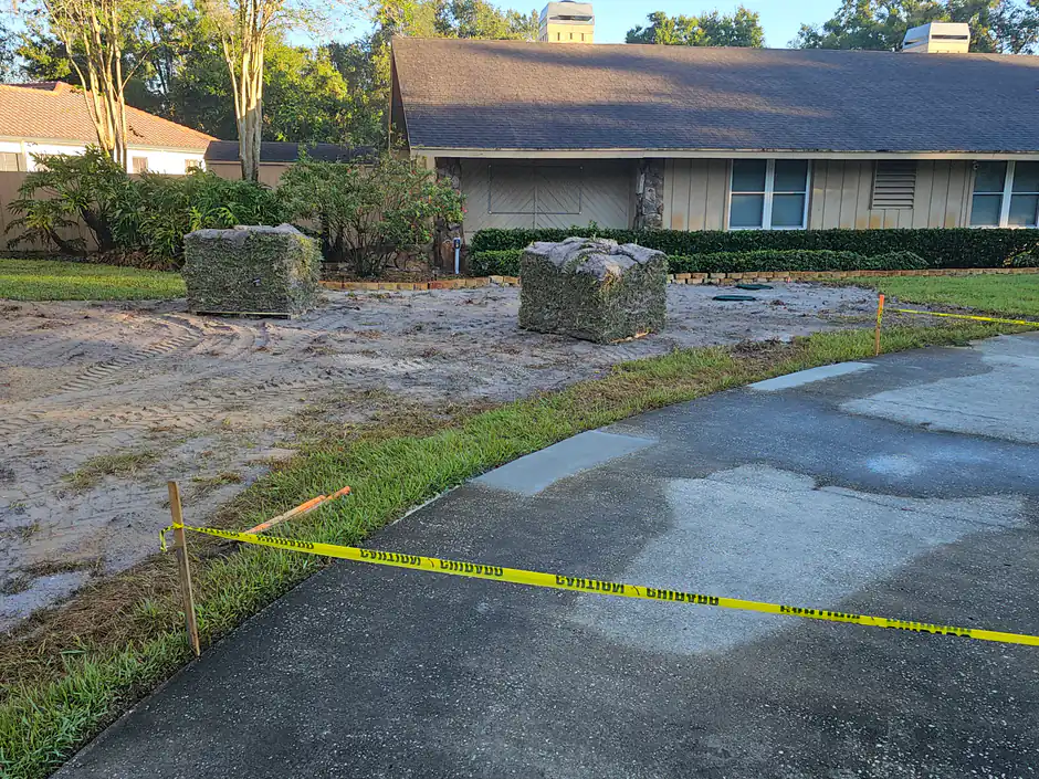 Pallets of fresh rolled sod staged on a graded front yard Woods prepped for a new sod installation